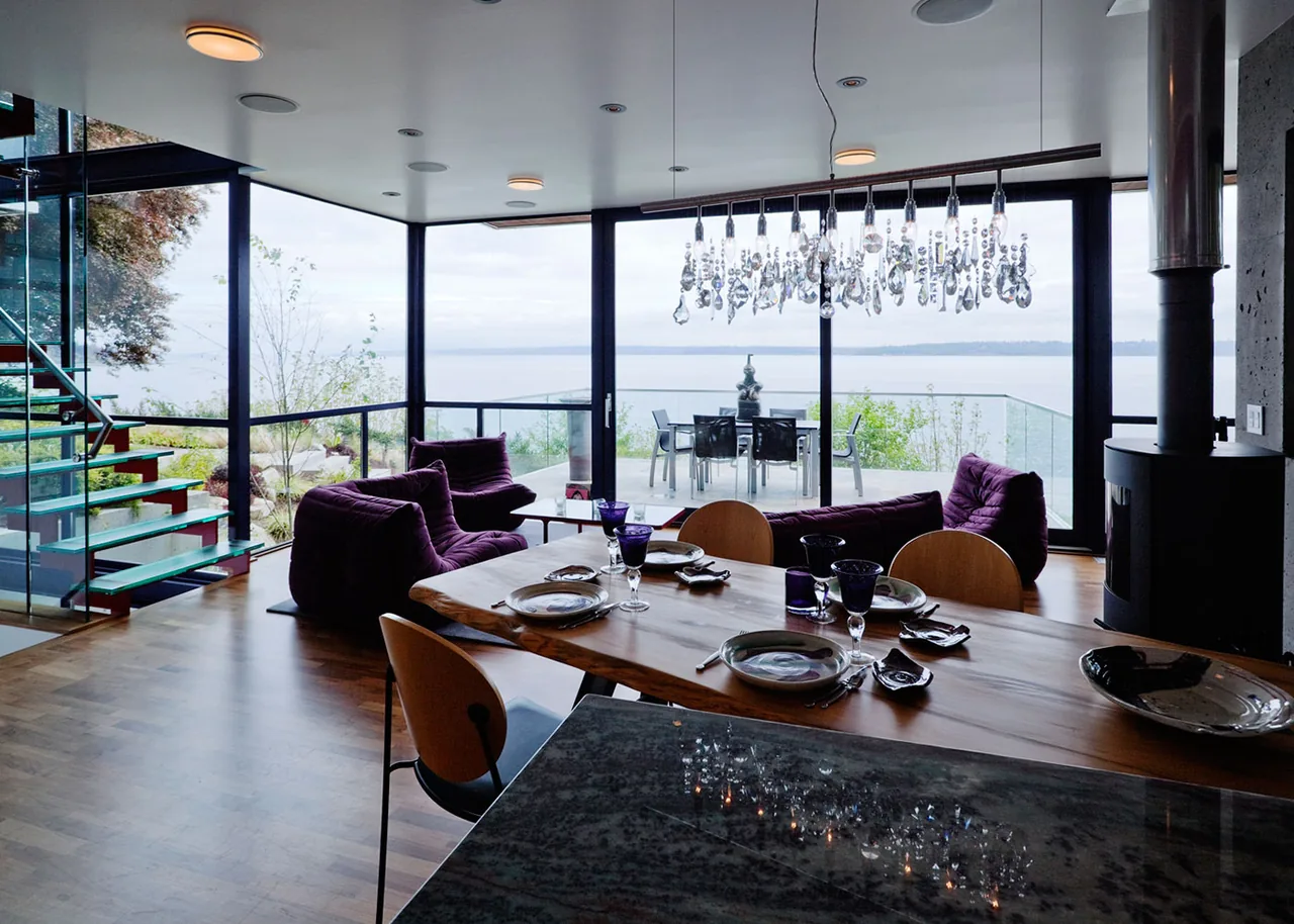 Dining and living area of Bainbridge Island Guest Residence with floor-to-ceiling glazing and a glass-railing balcony.