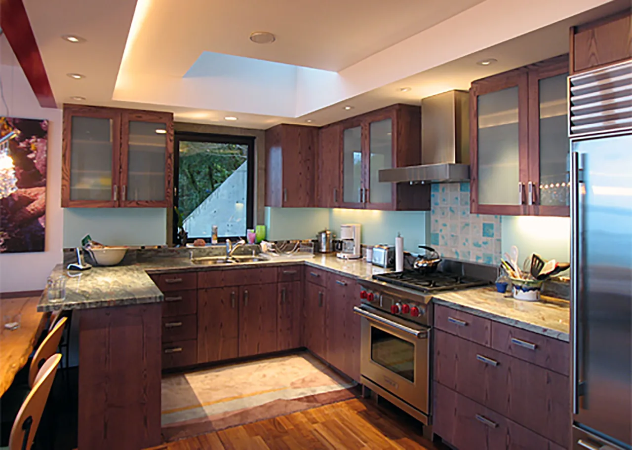 The Bainbridge Island Guest Residence kitchen features dark wood cabinetry, stainless steel appliances, and a central skylight.