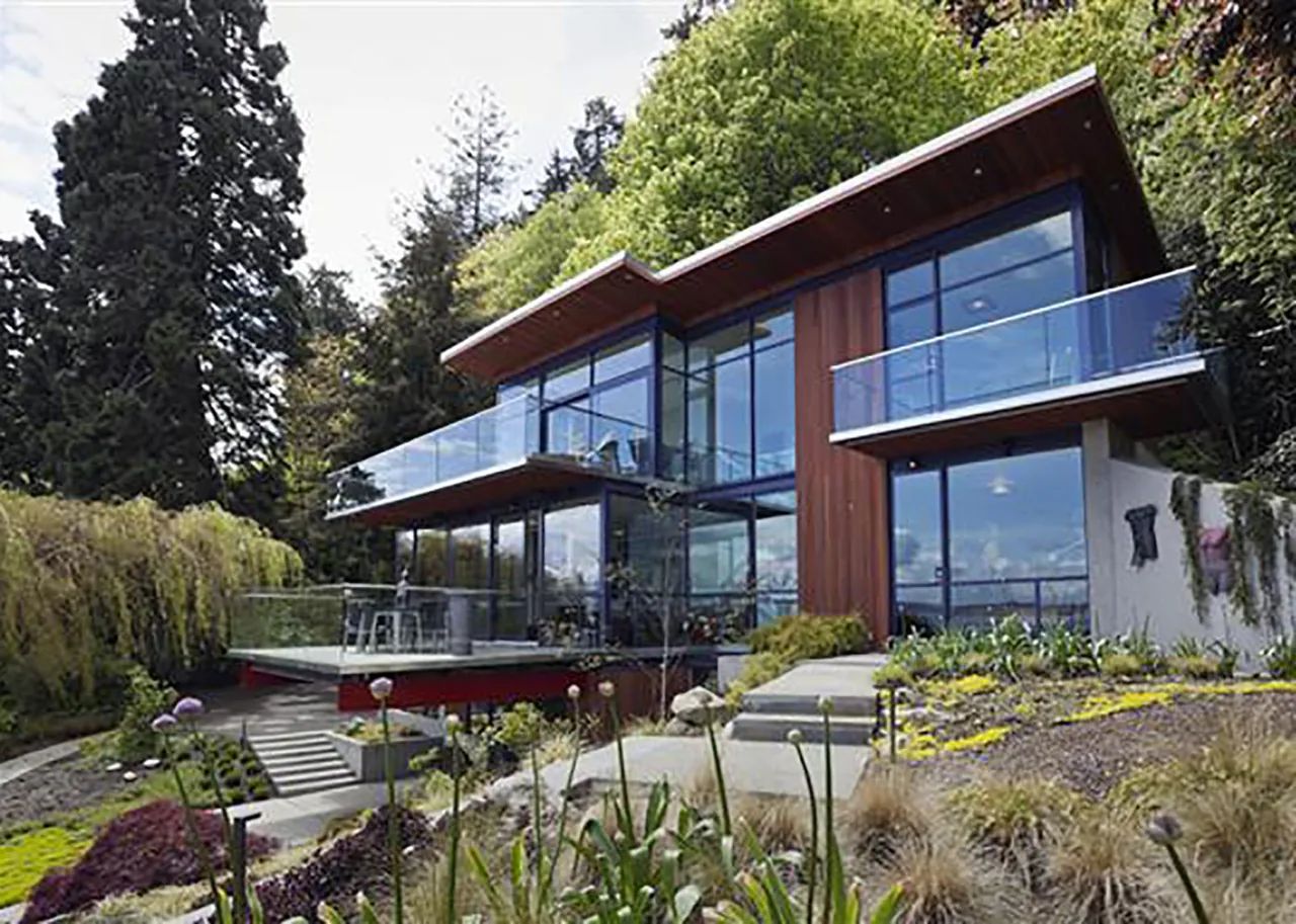 The Bainbridge Island Guest Residence features large glass walls and glass guardrails on its balconies, blending with the landscaped hillside.