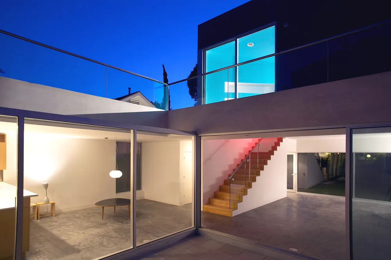 Sale House features large glass sliding doors and a wooden stair inside with bright interior lighting.