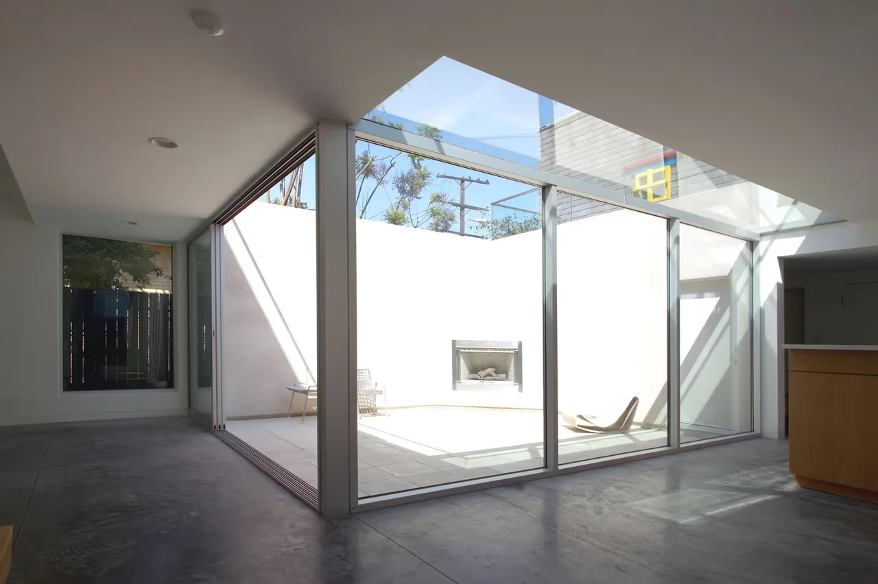 The Sale House courtyard features floor-to-ceiling sliding doors and an outdoor fireplace enclosed by white walls.