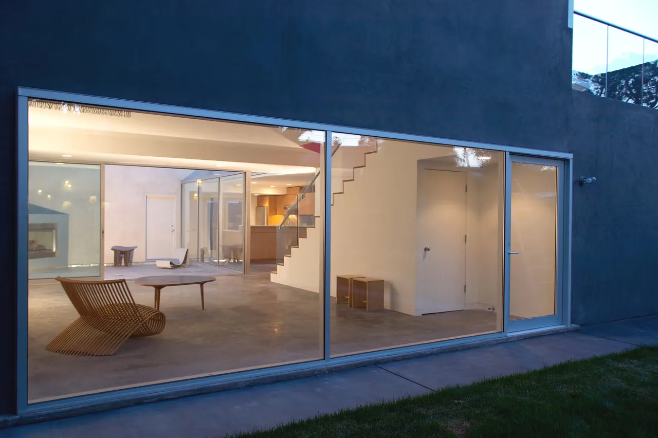 Exterior view of Sale House showcasing large floor-to-ceiling windows revealing minimal interior furniture and a staircase.