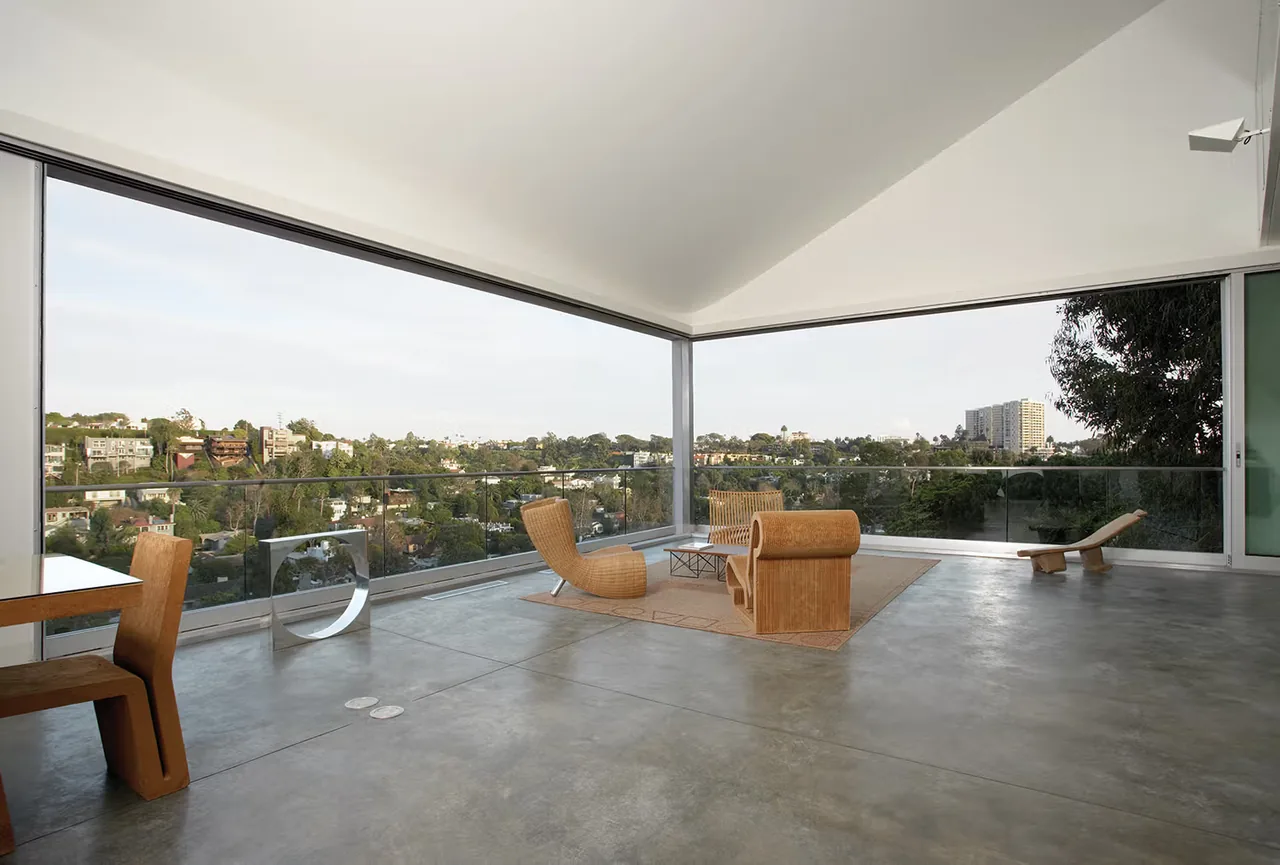 Covered outdoor living area at Hill House features concrete flooring and glass railing with city views.