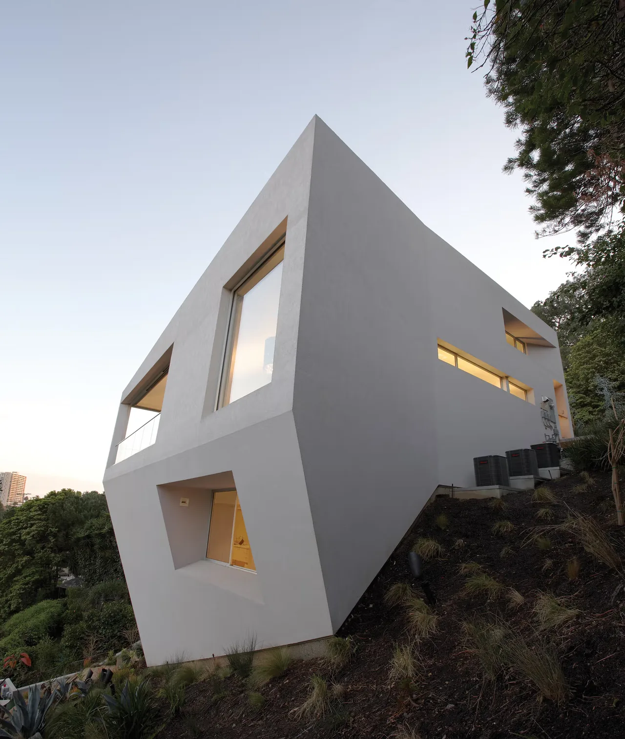 Hill House features a white angular modern exterior with large cutout windows and glass railings on a sloped site.