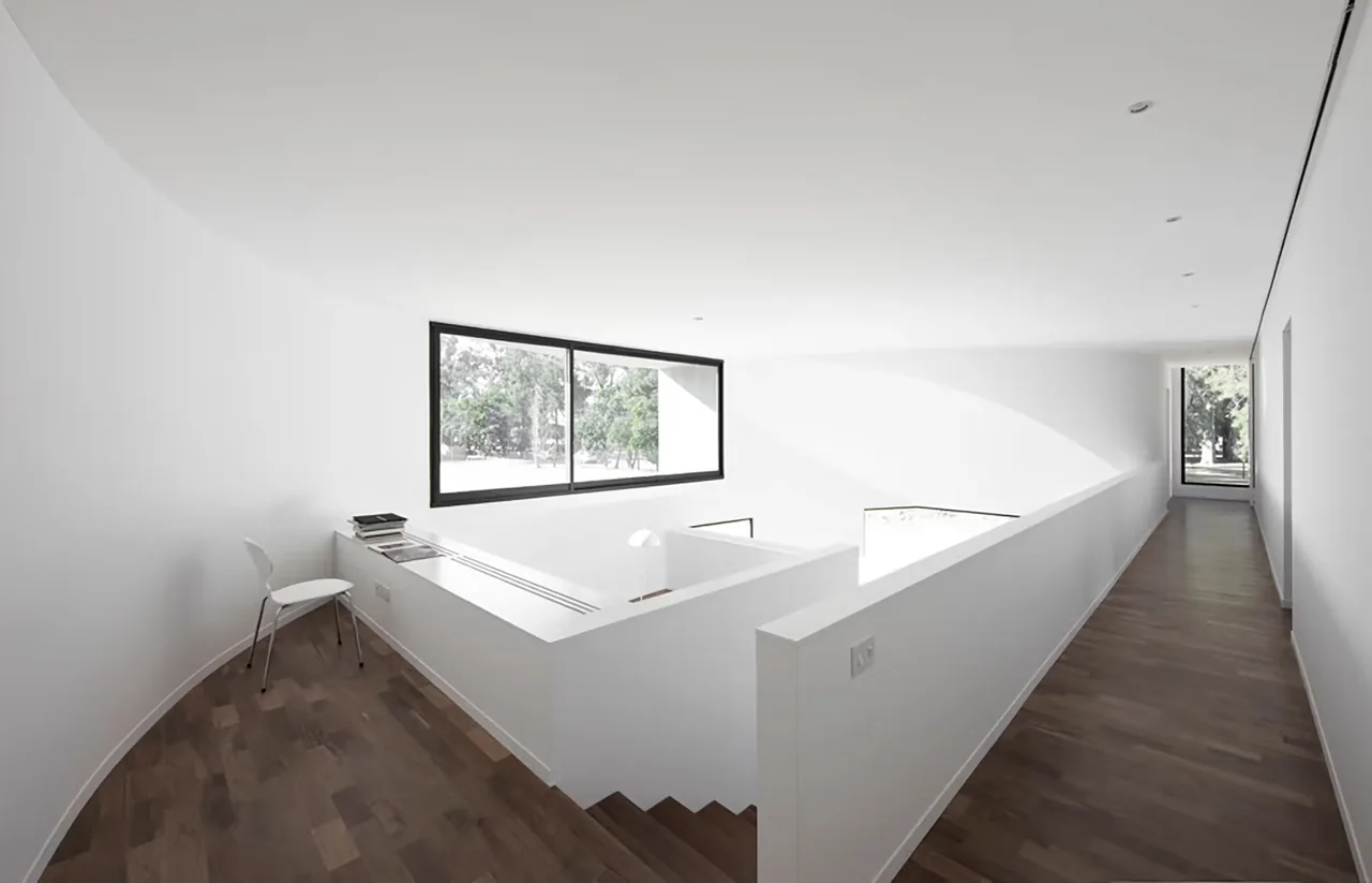 Curved interior hallway with wooden flooring and a large black-framed window at View House in Los Angeles.