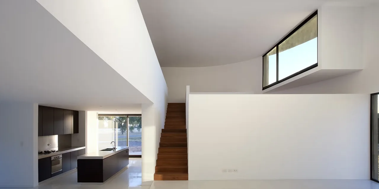 Minimalist interior with wood stairs, black kitchen cabinetry, and large black-framed windows above and beside the stairwall.