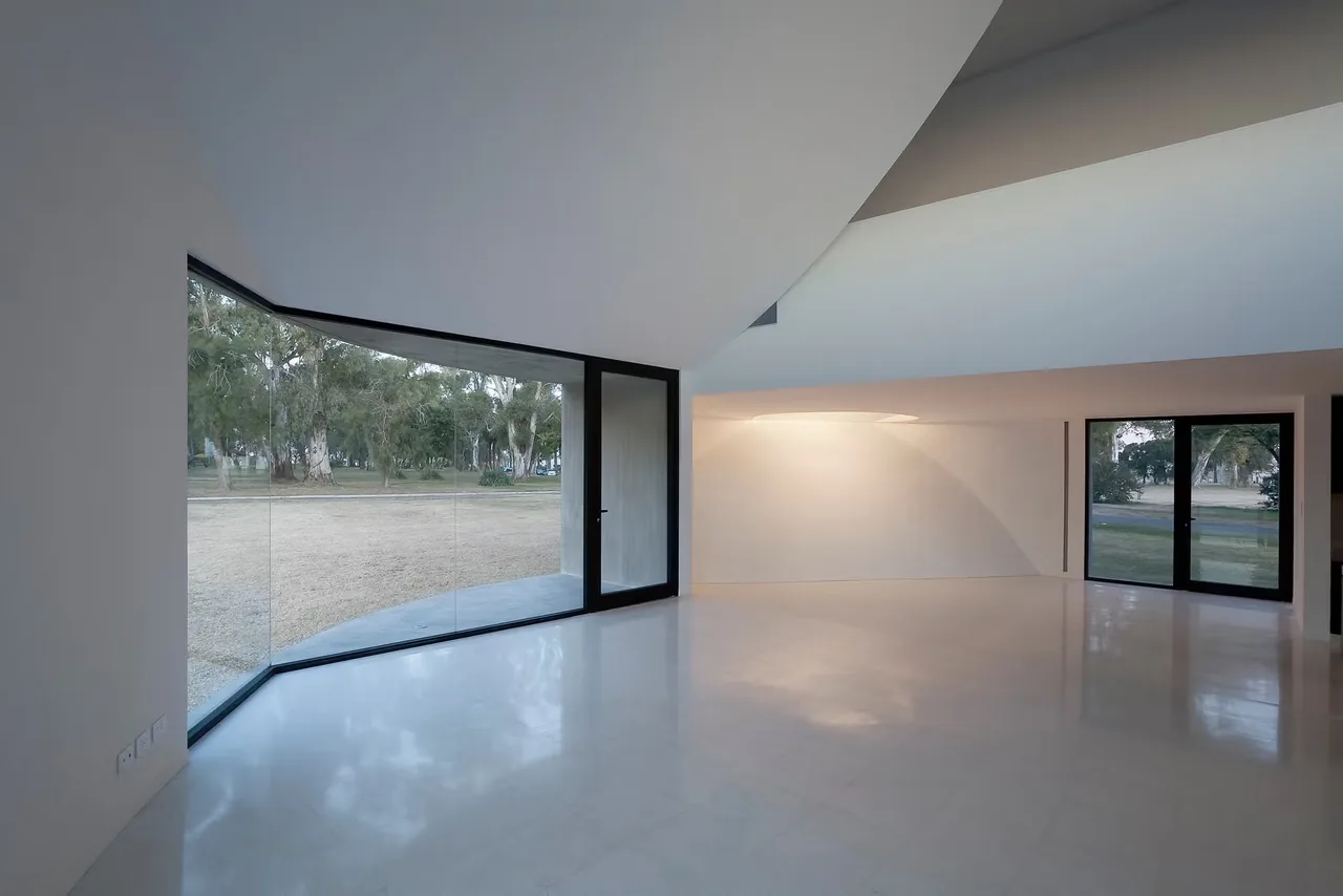 View House features a minimalist interior with expansive curved floor-to-ceiling glazing overlooking the yard.