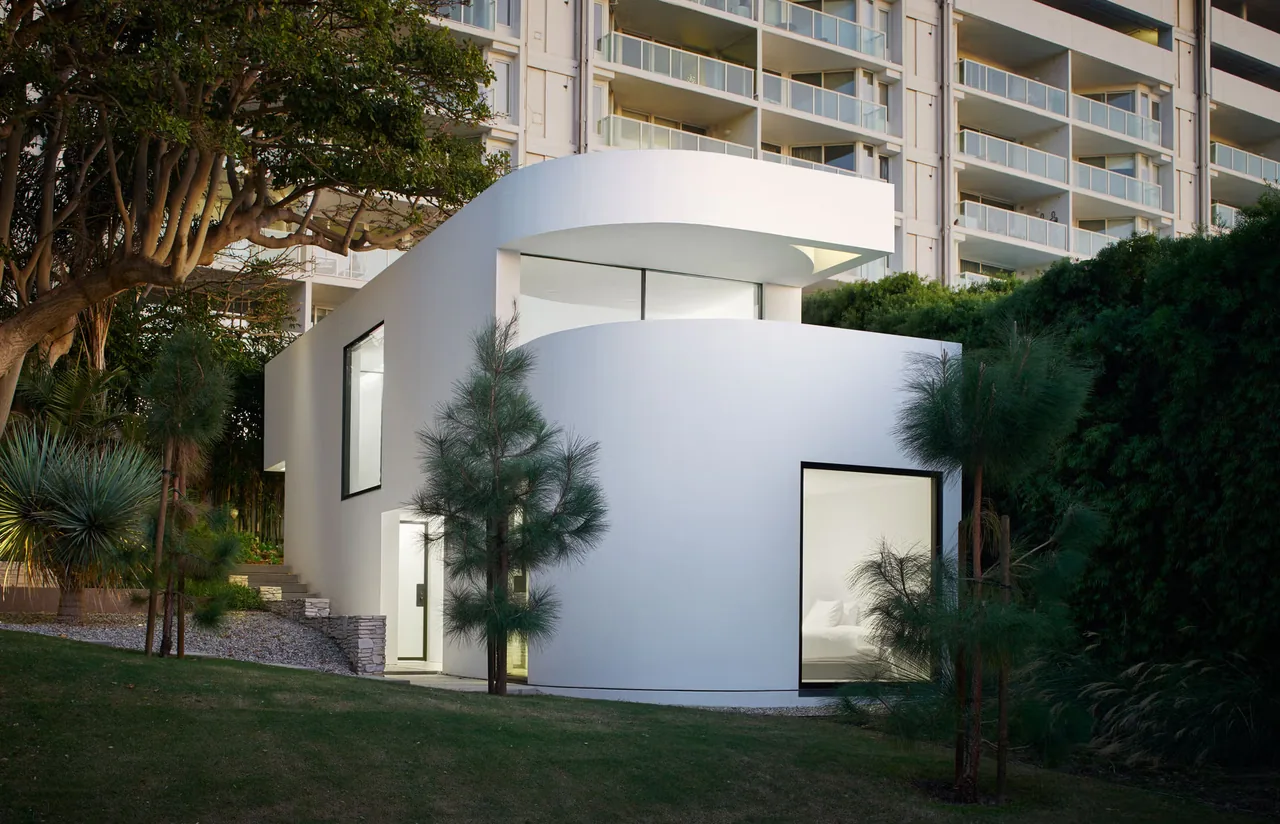 Modern white curved and rectilinear residential building with large black-framed windows beside greenery.