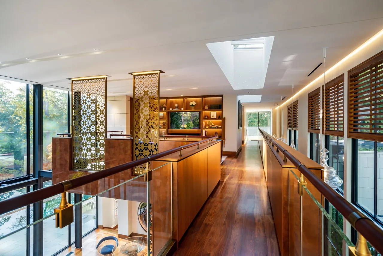 Upstairs hallway features wood flooring, skylights, glass and wood balustrades, with views into a living area with built-in shelves.
