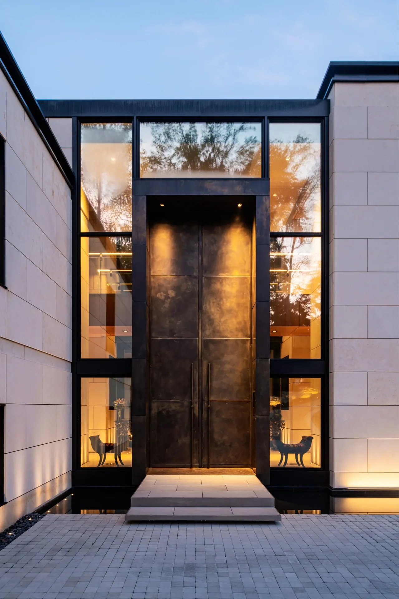 The entry of VILLA VIRGINIA features a tall black metal door surrounded by expansive glass panels and light stone walls.