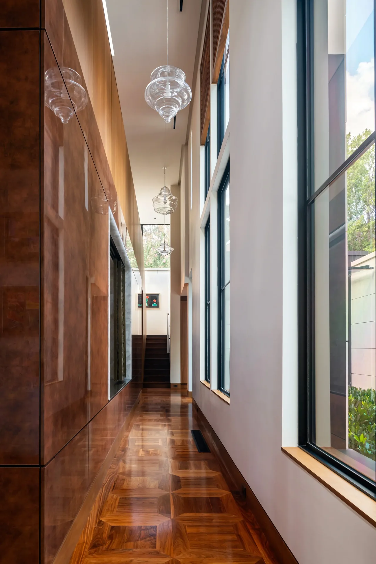 Hallway features high ceilings, parquet wood flooring, and large windows with black frames letting in natural light.