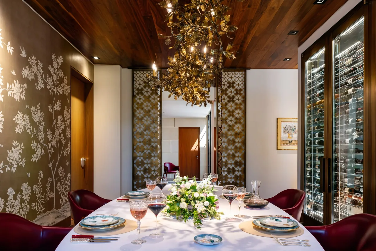 Villa Virginia dining room features a white tablecloth set table, dark red chairs, decorative wall panels, and a wine storage cabinet.