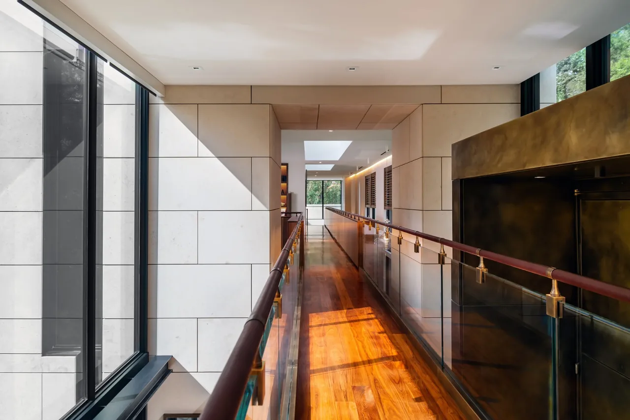 Interior hallway features glass railing and wood floors with wall cladding and skylight above.