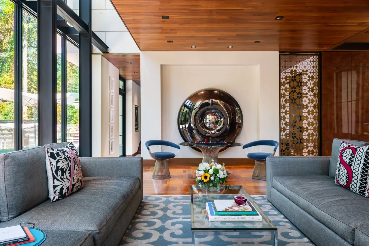 Villa Virginia living room featuring floor-to-ceiling windows, wood paneled ceiling, and a large reflective circular art piece on the wall.