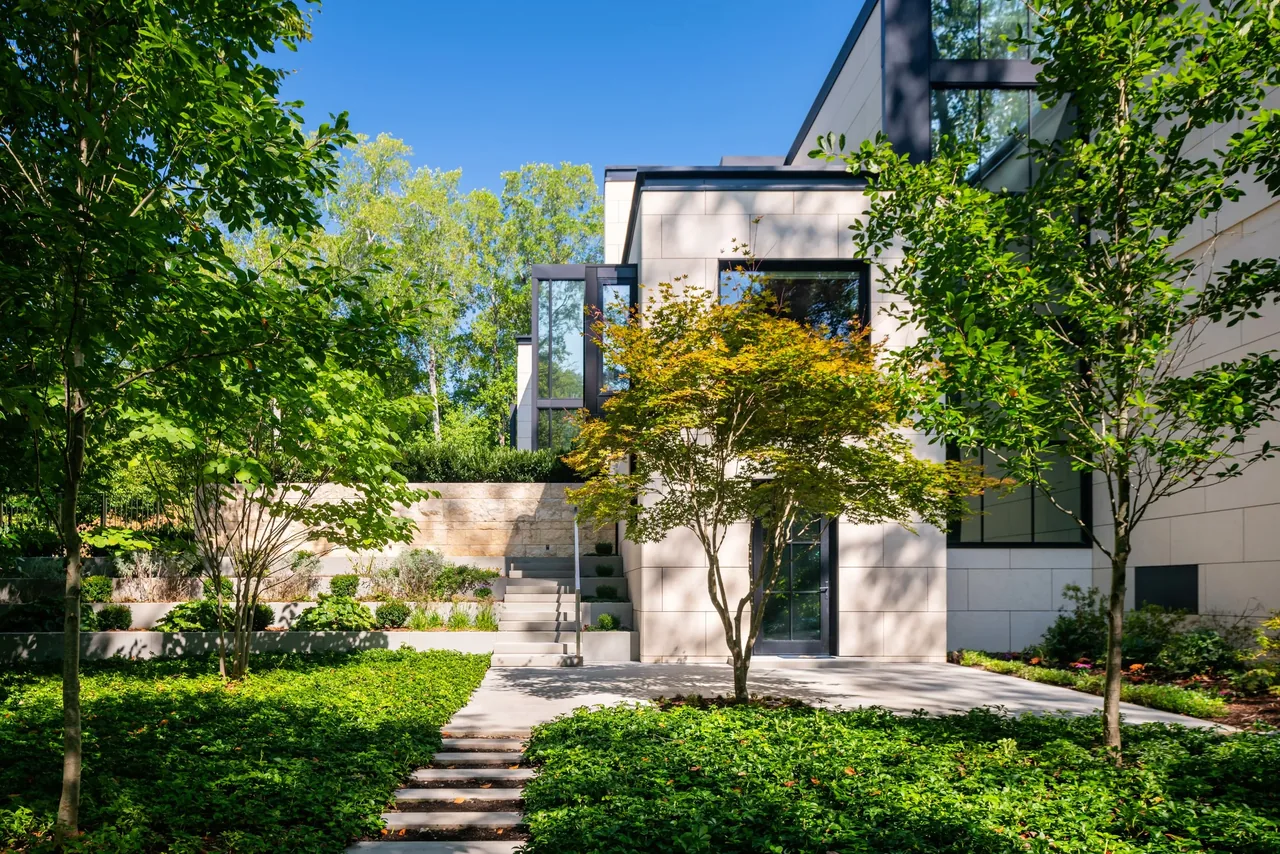 Modern house exterior featuring stone cladding and landscaped courtyard with stairs and greenery.