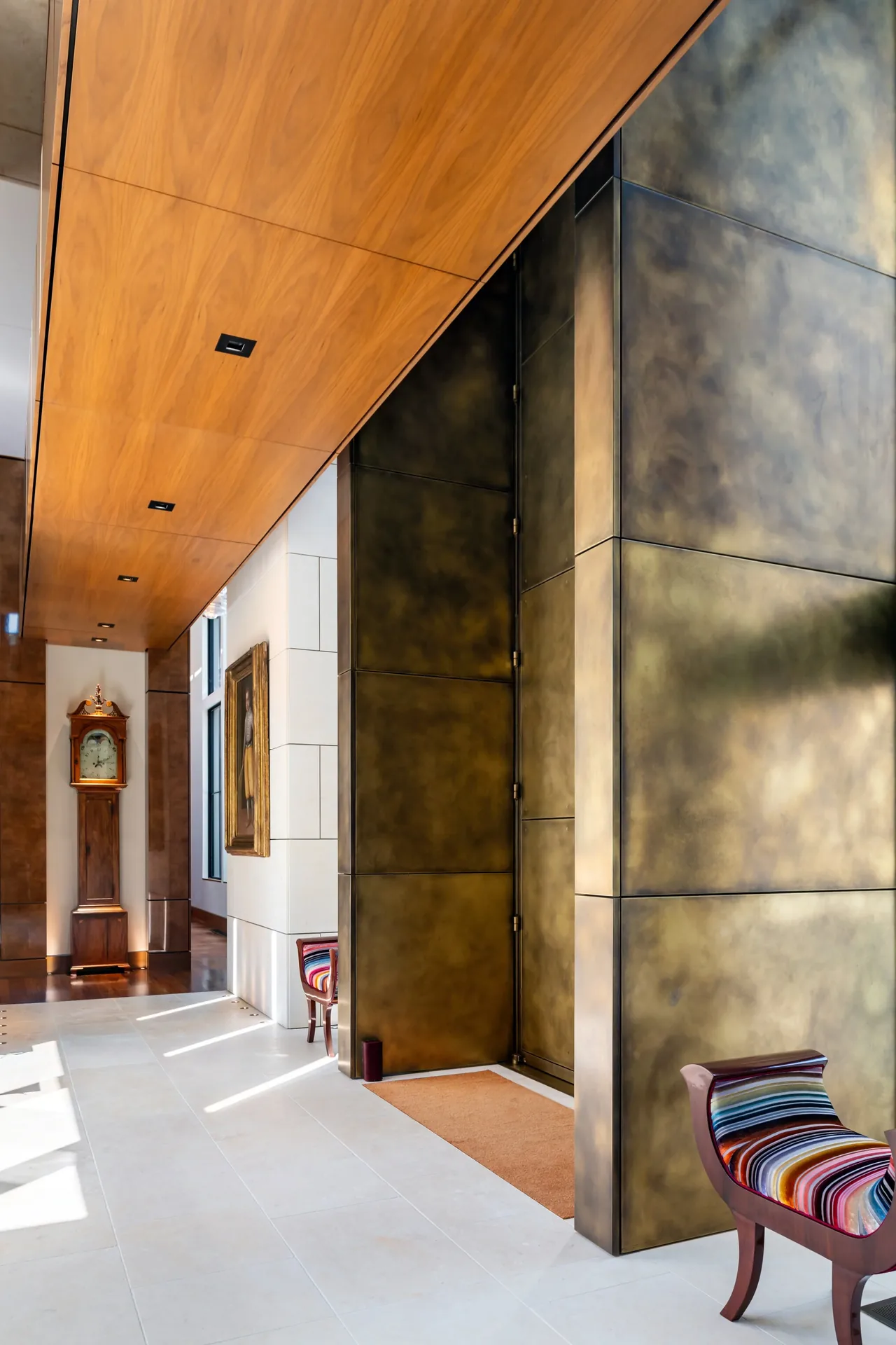 The entry features a large metal-paneled pivot door with wood-paneled ceiling and tile floor.