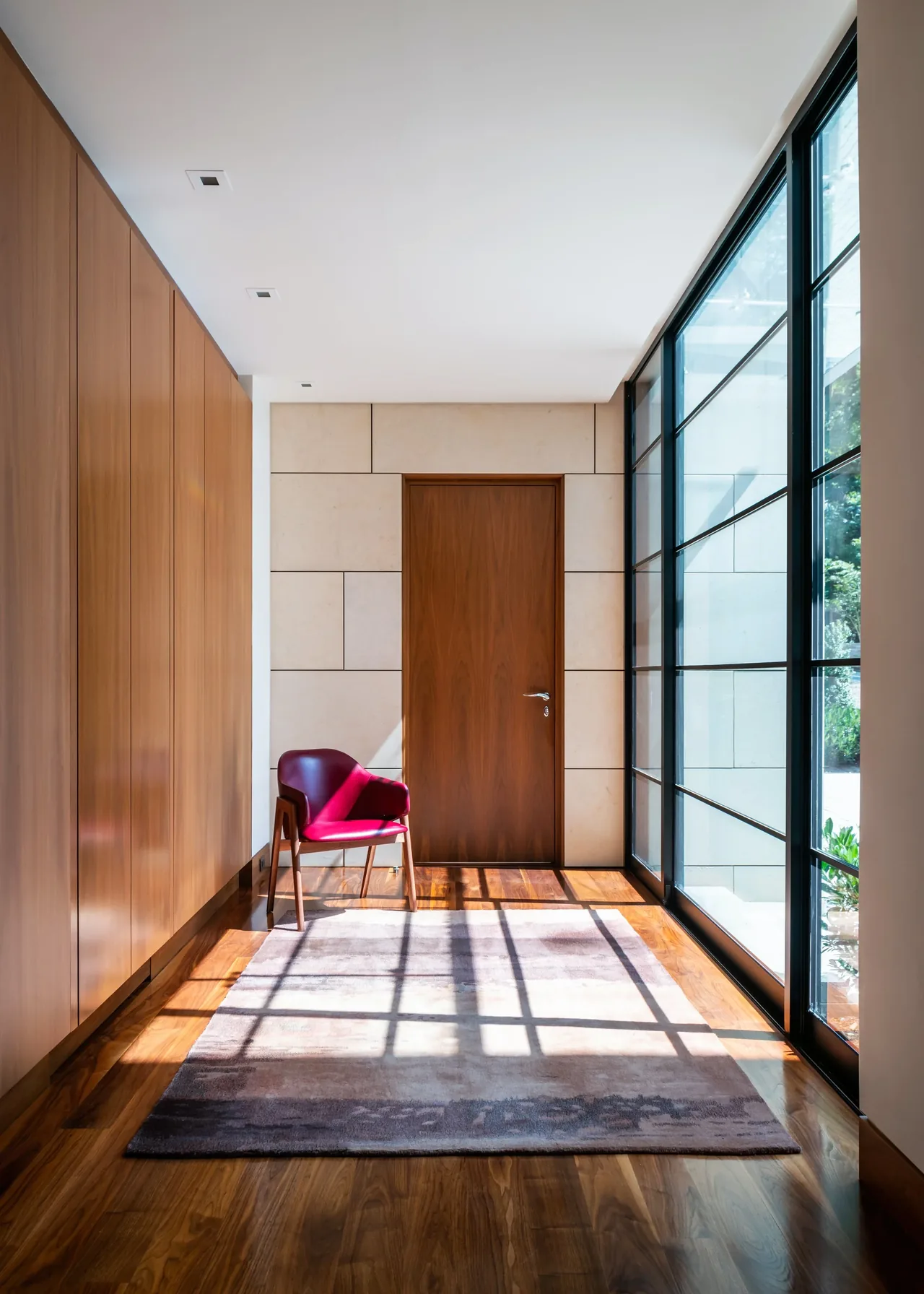 Hallway with wood flooring, wooden door, and floor-to-ceiling black-framed windows on one side.