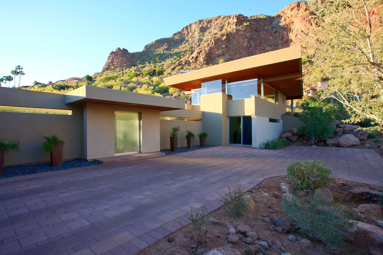 Monks Shadow Residence features flat roofs, stucco walls, and large glass windows integrated into a desert mountain landscape.
