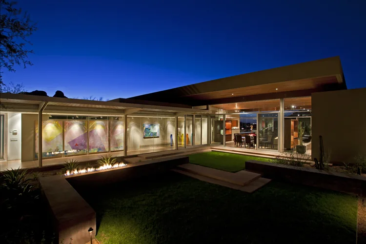 Monks Shadow Residence with floor-to-ceiling glazing and integrated desert landscaping under a flat roof at dusk.