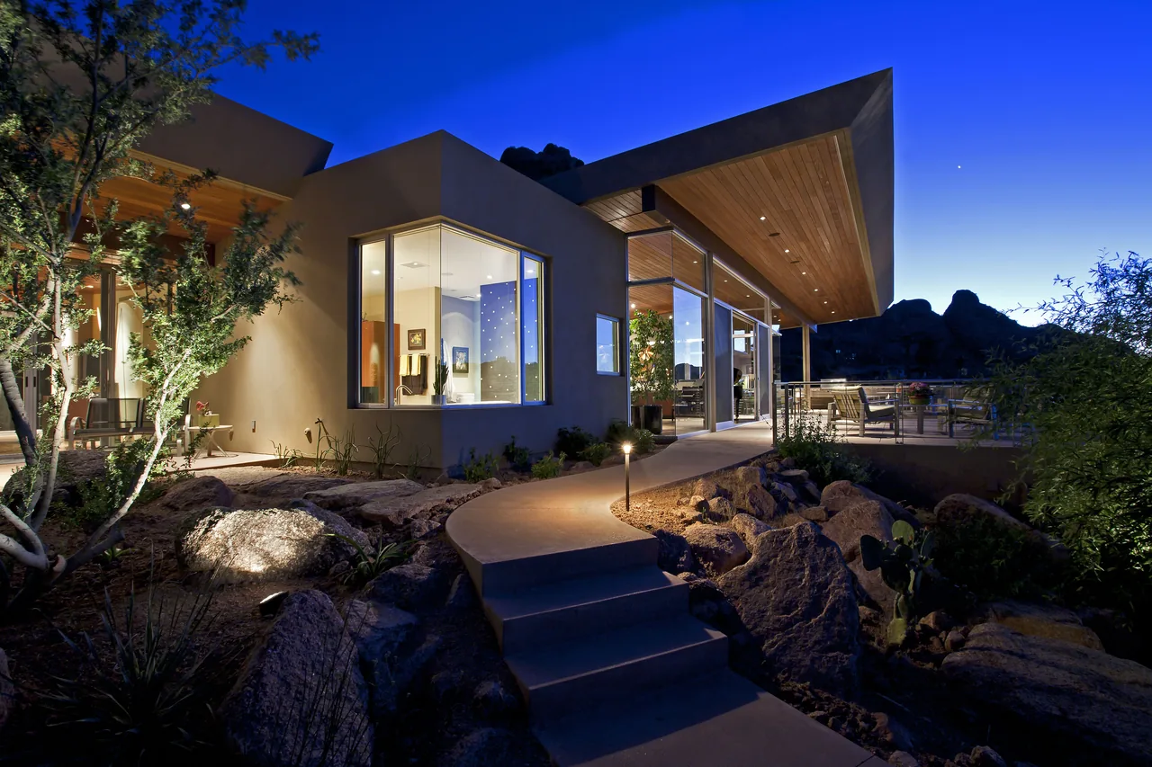 Monks Shadow Residence features a modern angled roof, wood-paneled ceiling, and desert landscaping with rocky hillside views.