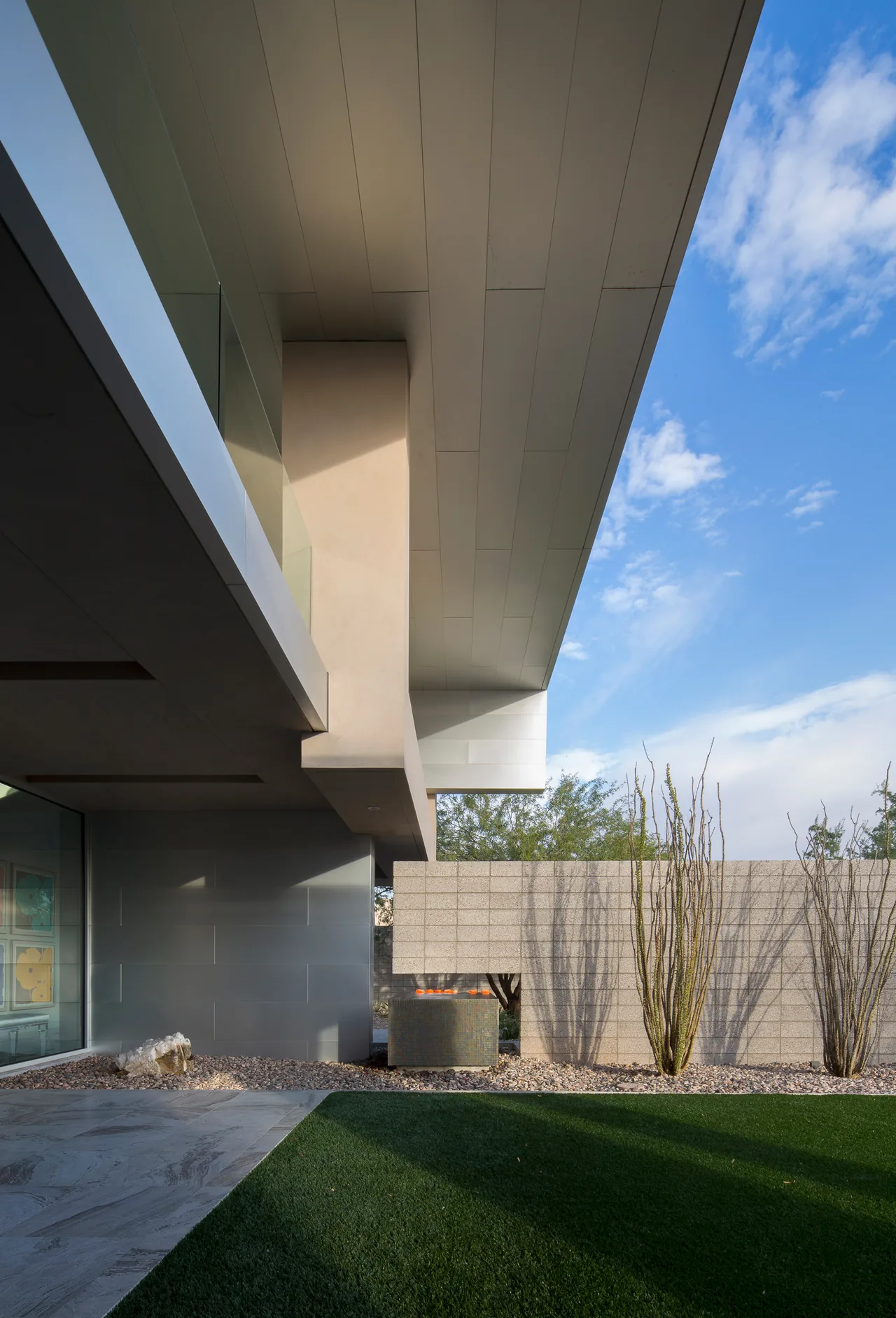 Modern exterior view showing a cantilevered roof above an outdoor area with desert landscaping and a concrete block wall.