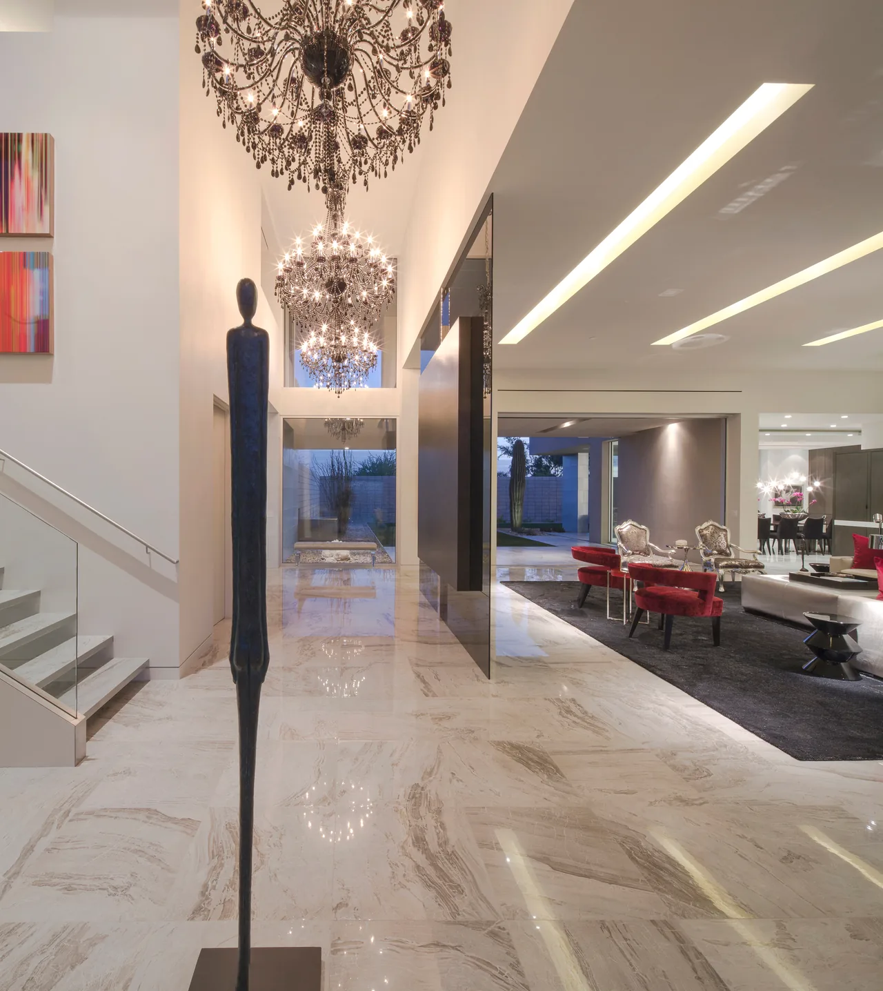 Entry hallway with chandeliers and marble tile flooring leading to a modern living room with red and white seating.