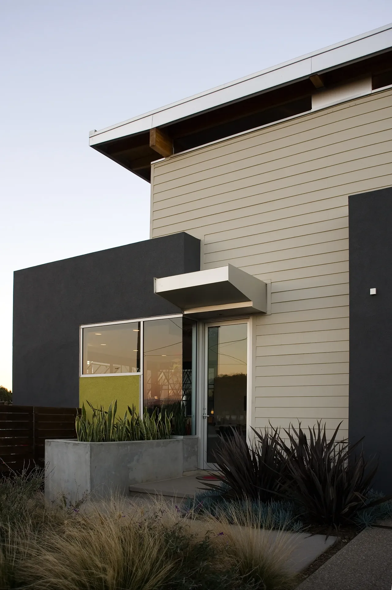 Casa Familia entrance features beige siding with dark stucco accents and a glass door under a small metal canopy.