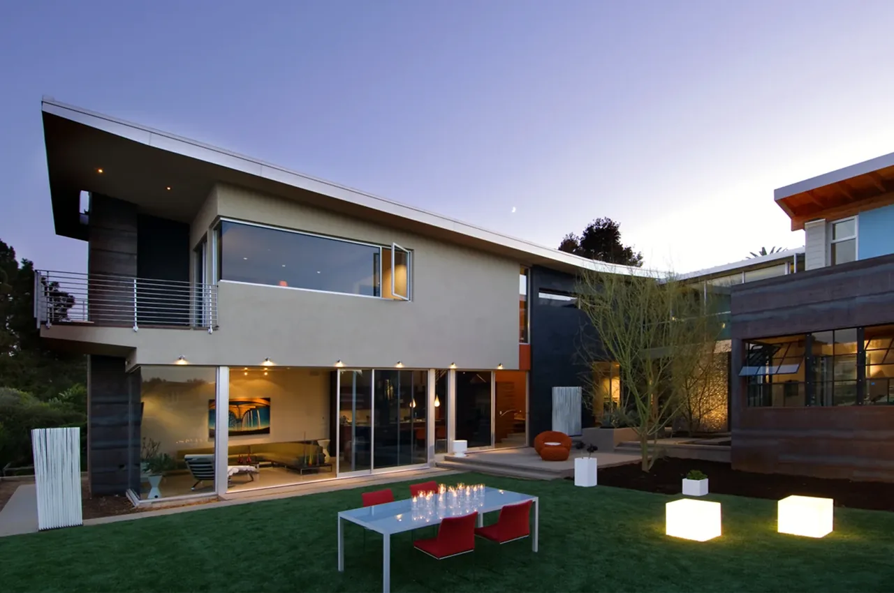 Casa Familia by Kevin deFreitas Architects features a modern exterior with extensive glazing and outdoor seating on an evening lawn.