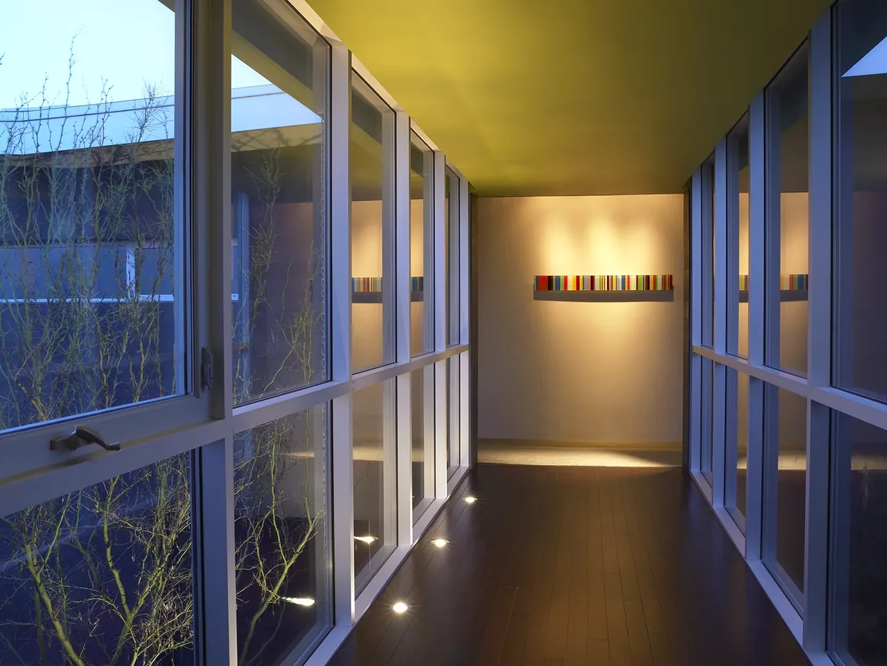 Corridor with floor-to-ceiling glazing and a green painted ceiling illuminated at night.