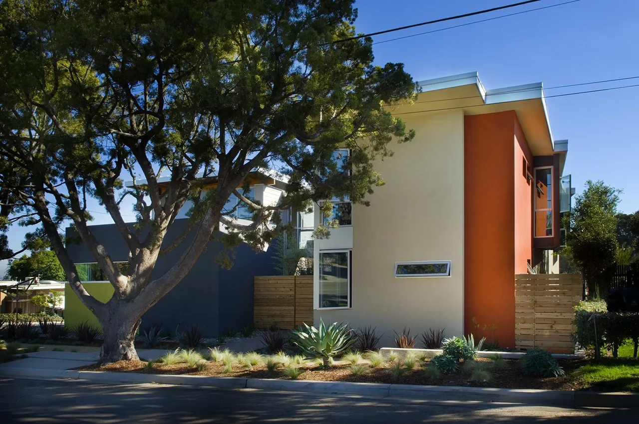 Exterior front view of Casa Familia, a modern home with beige, orange, and dark gray walls and a flat roof by Kevin deFreitas Architects.