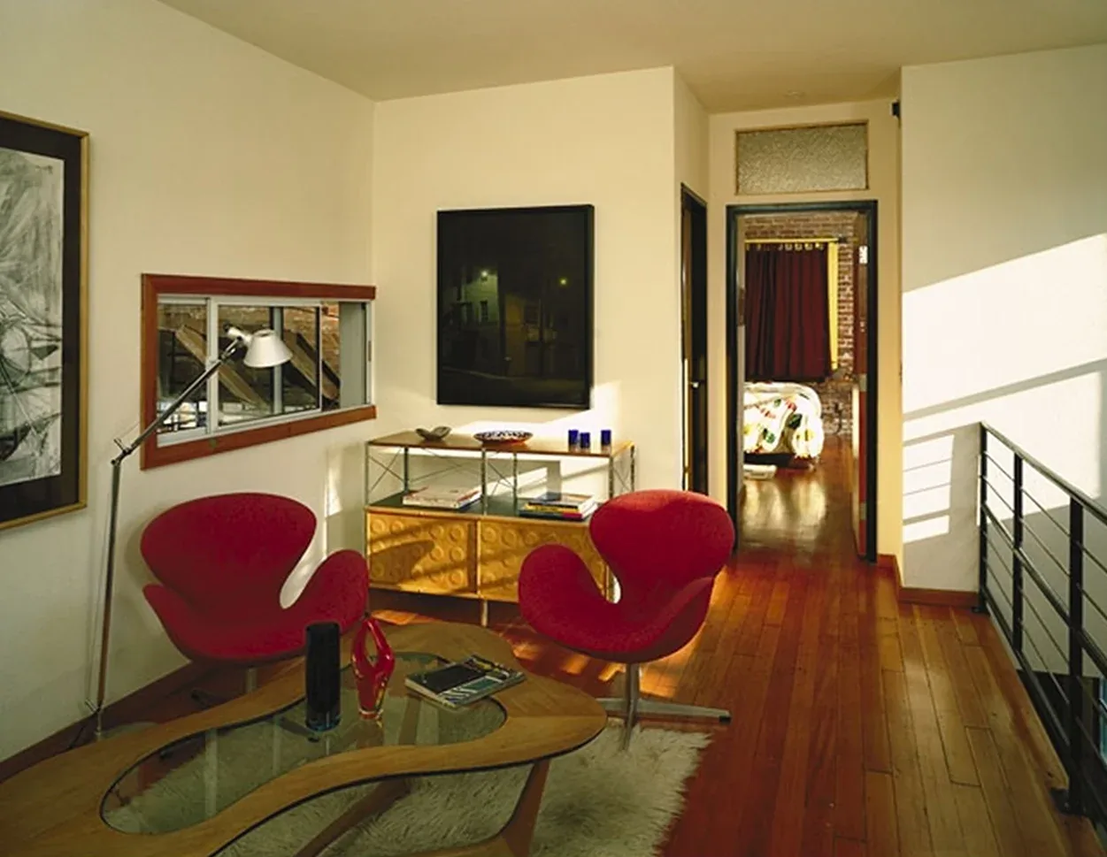 Waltmon Lofts features a hallway with wood floors, red seating, and a glimpse into a bedroom with exposed brick and dark curtains.