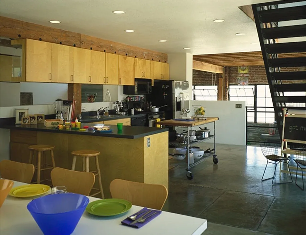 Waltmon Lofts kitchen features wooden cabinetry, concrete floors, and an open layout with a dining table and metal staircase.