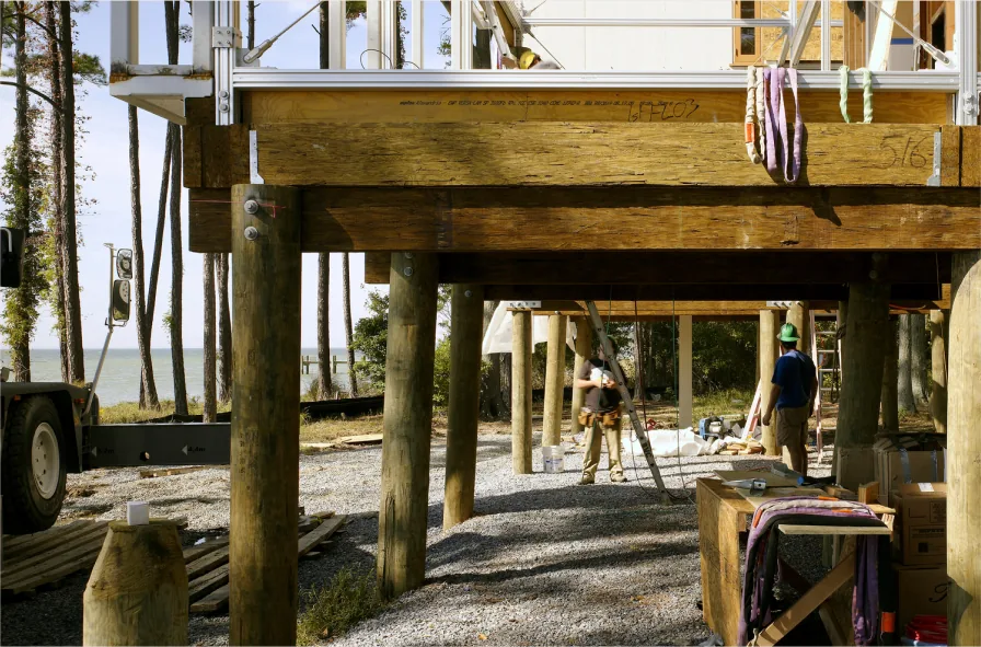 Wood-framed house foundation raised on wooden pilings during construction near waterfront.