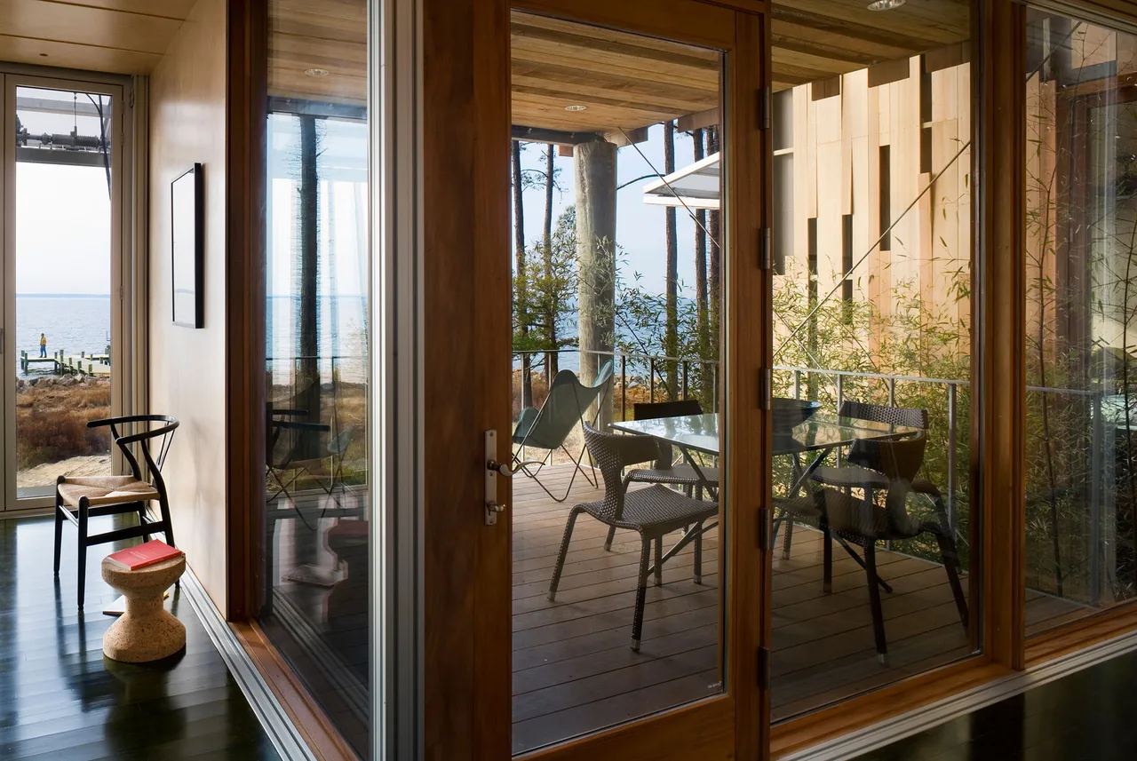 Glass door connects an interior room to an outdoor covered patio with seating and a waterfront view.