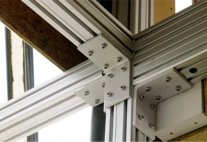 Metal joint bracket fastening aluminum structural extrusions in a building's corner detail.