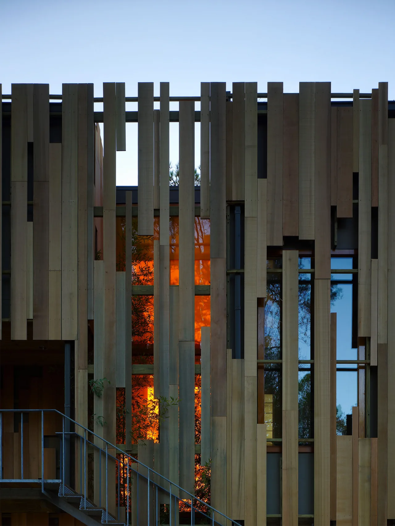 Exterior view of Loblolly House features vertical wood paneling with dimensional wooden slats and a metal staircase railing.