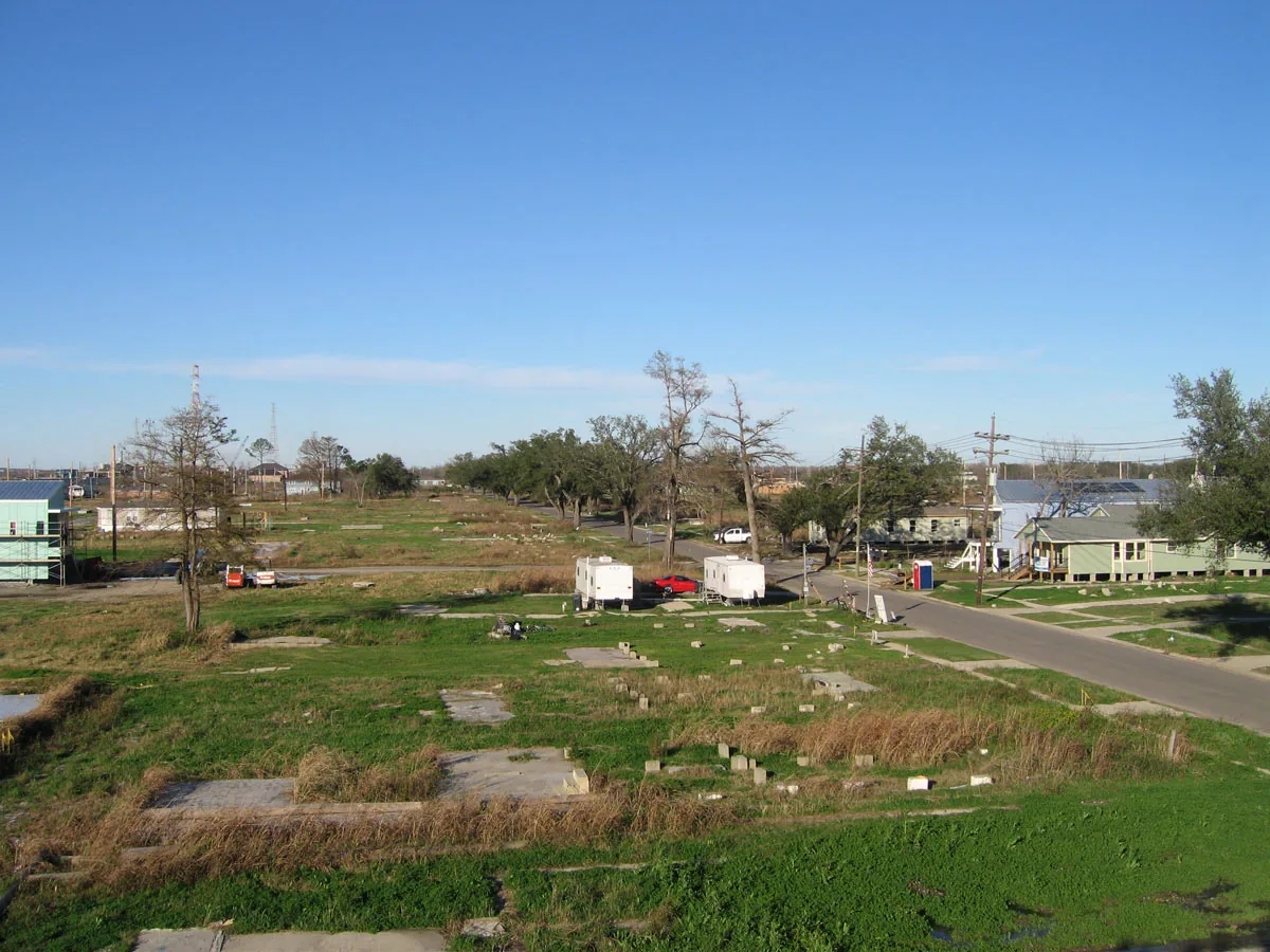 Site with grassy plots and concrete slabs near a road with scattered small houses and trailers.