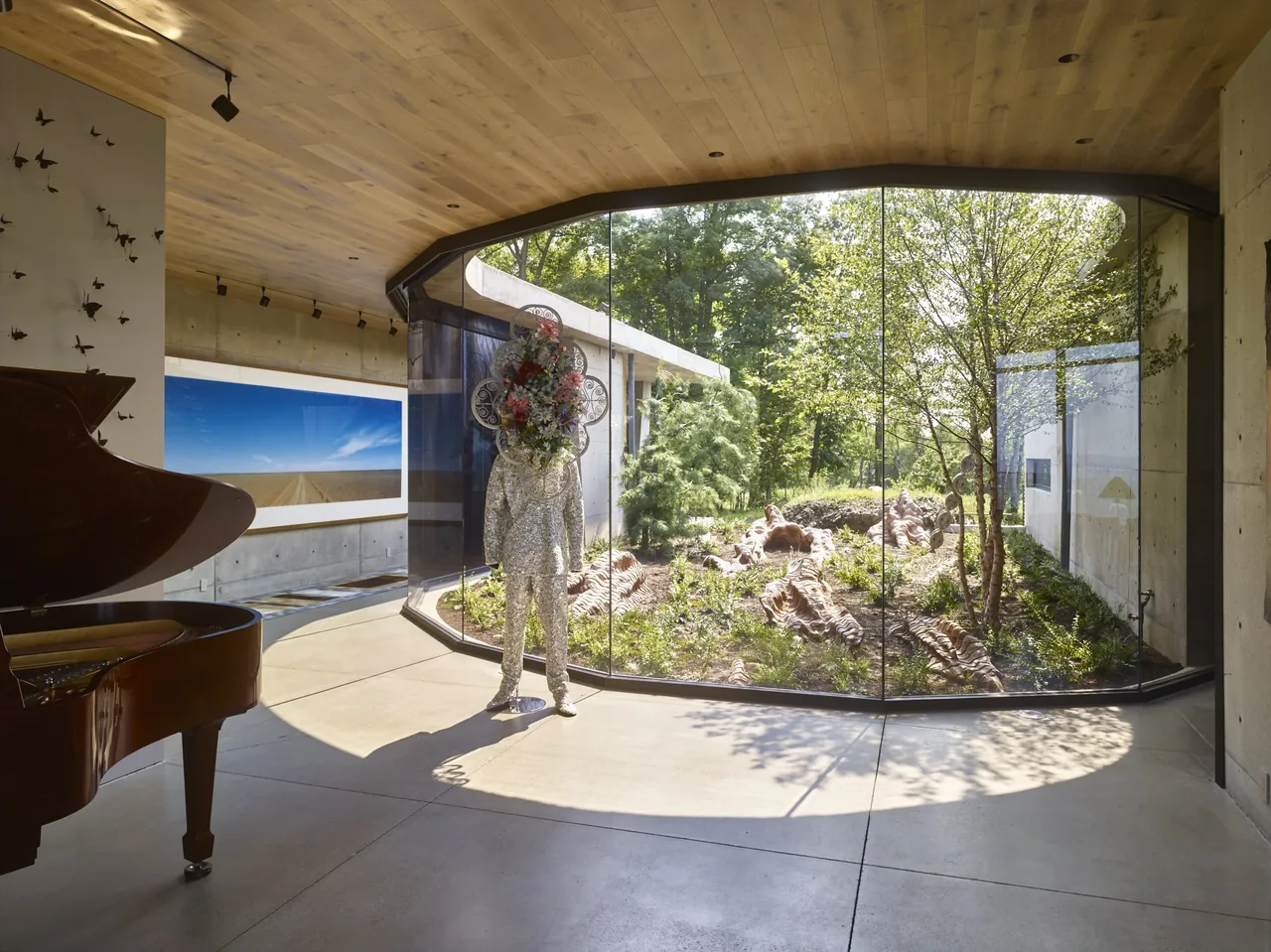 Hudson Concrete House features an interior view with a curved glass wall enclosing a garden, a piano, and artistic sculptures.