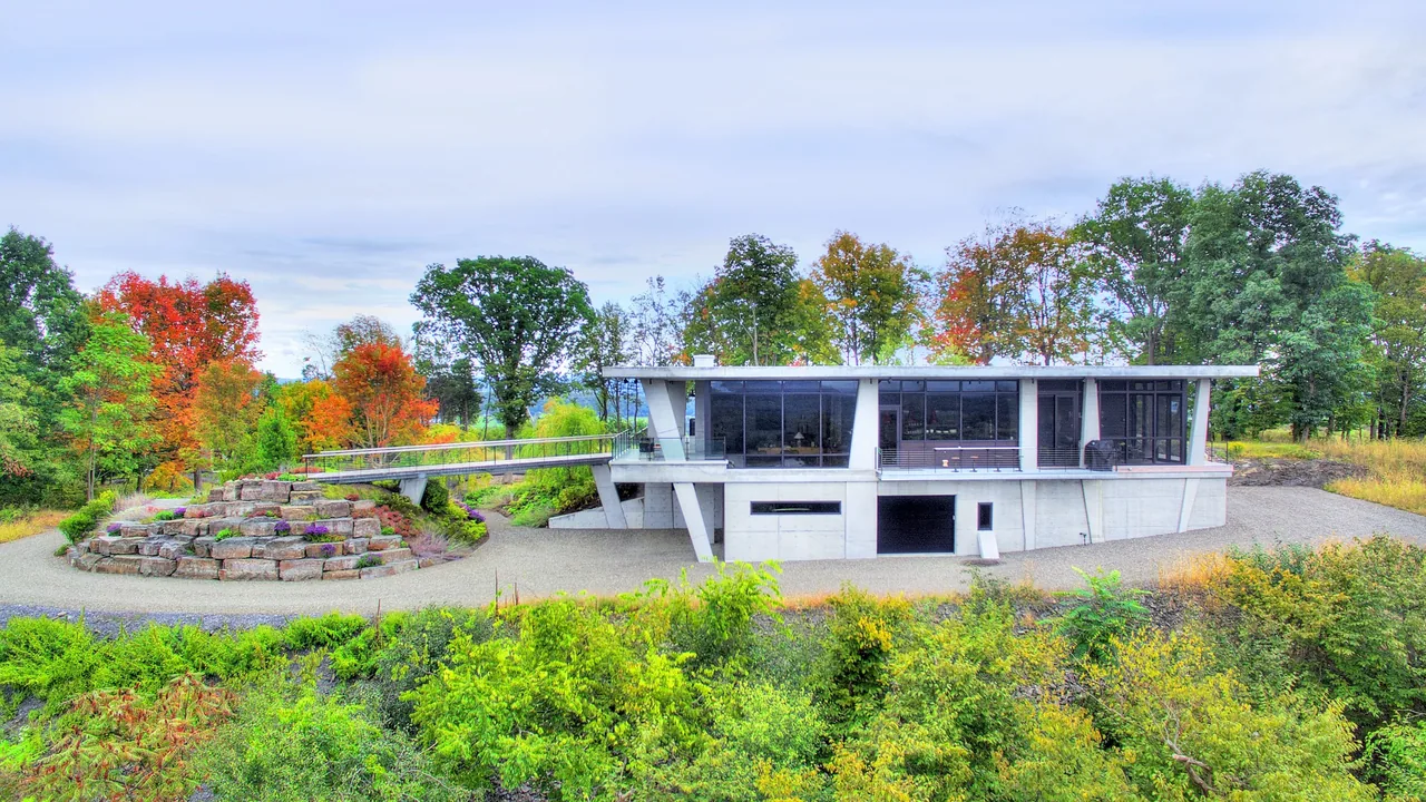 Hudson Concrete House features an elevated structure with large glass walls and a concrete base surrounded by fall foliage.