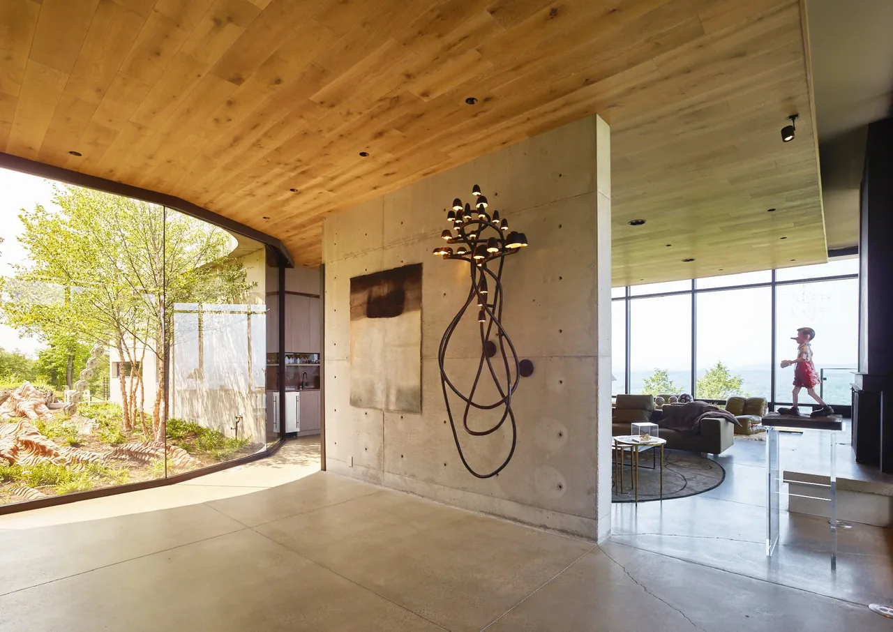 The Hudson Concrete House features a curved glass wall overlooking an indoor garden and a concrete wall with unique sculptural lighting.