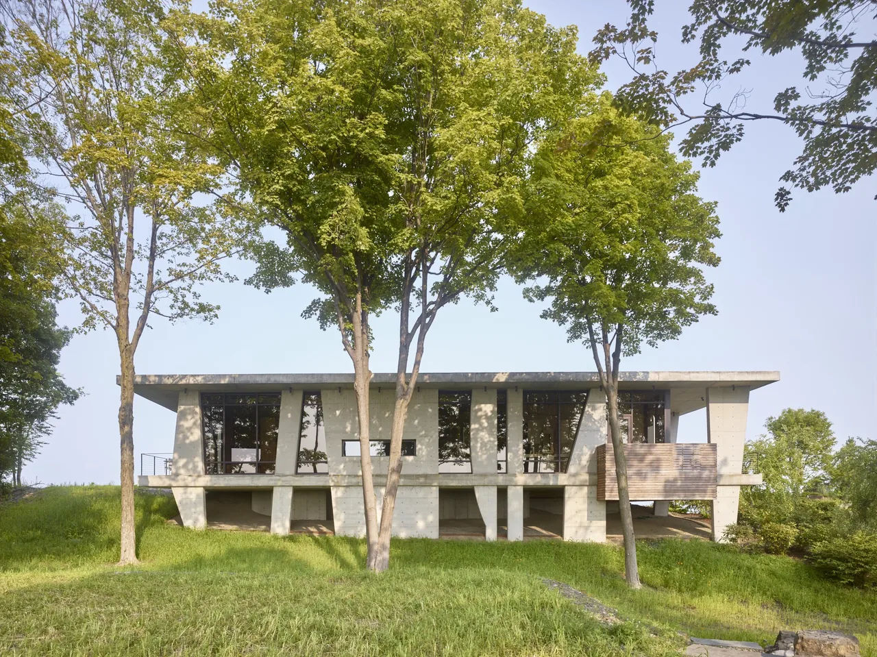 Hudson Concrete House features an elevated concrete structure with large windows and is surrounded by mature trees.