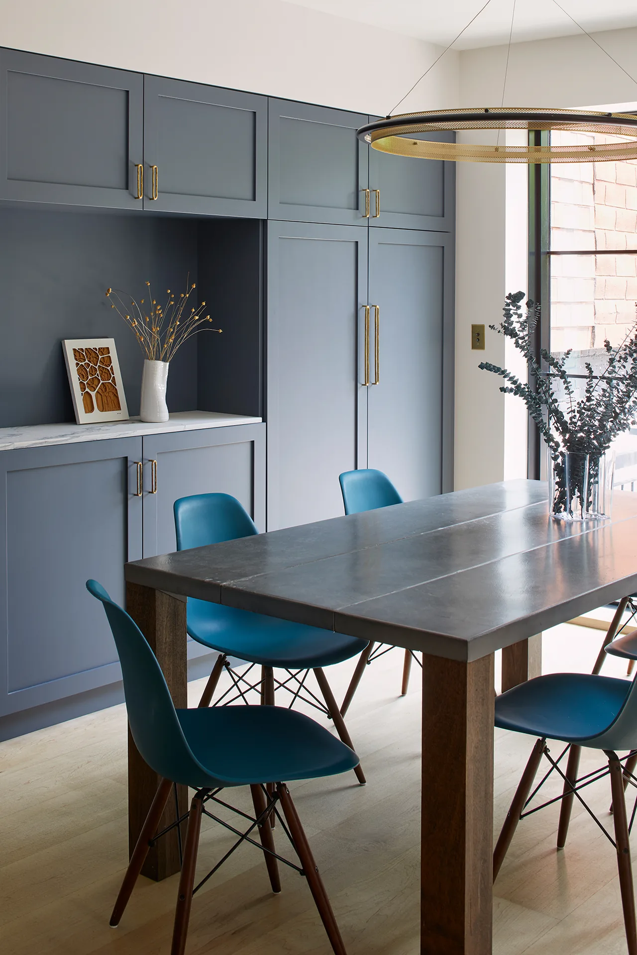 Dining space in the Greenpoint Residence featuring blue-gray built-in cabinets and a dark wood table with blue molded chairs.