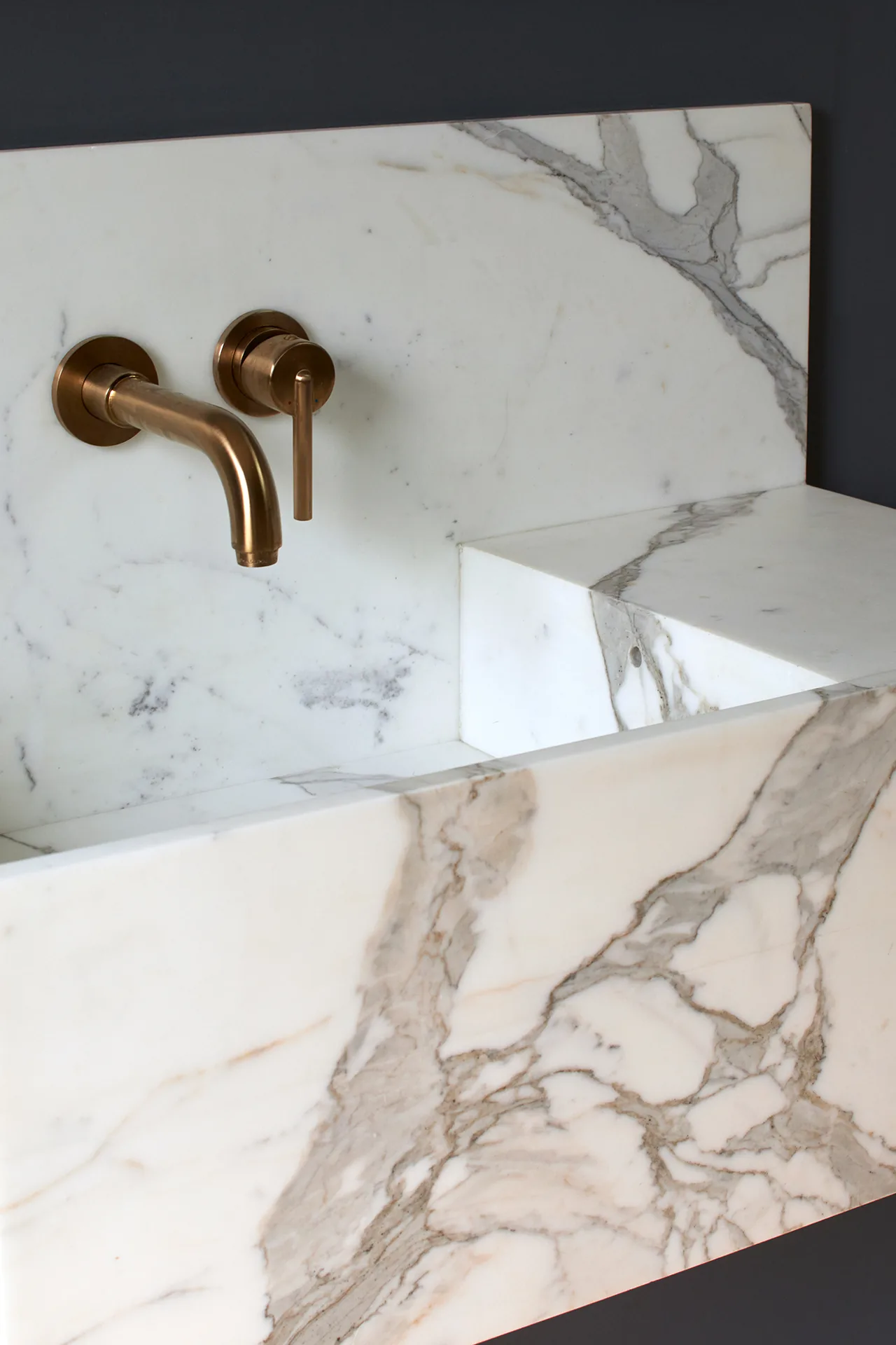 Rectangular white marble sink with prominent gray veining and brass wall-mounted faucet in a bathroom.
