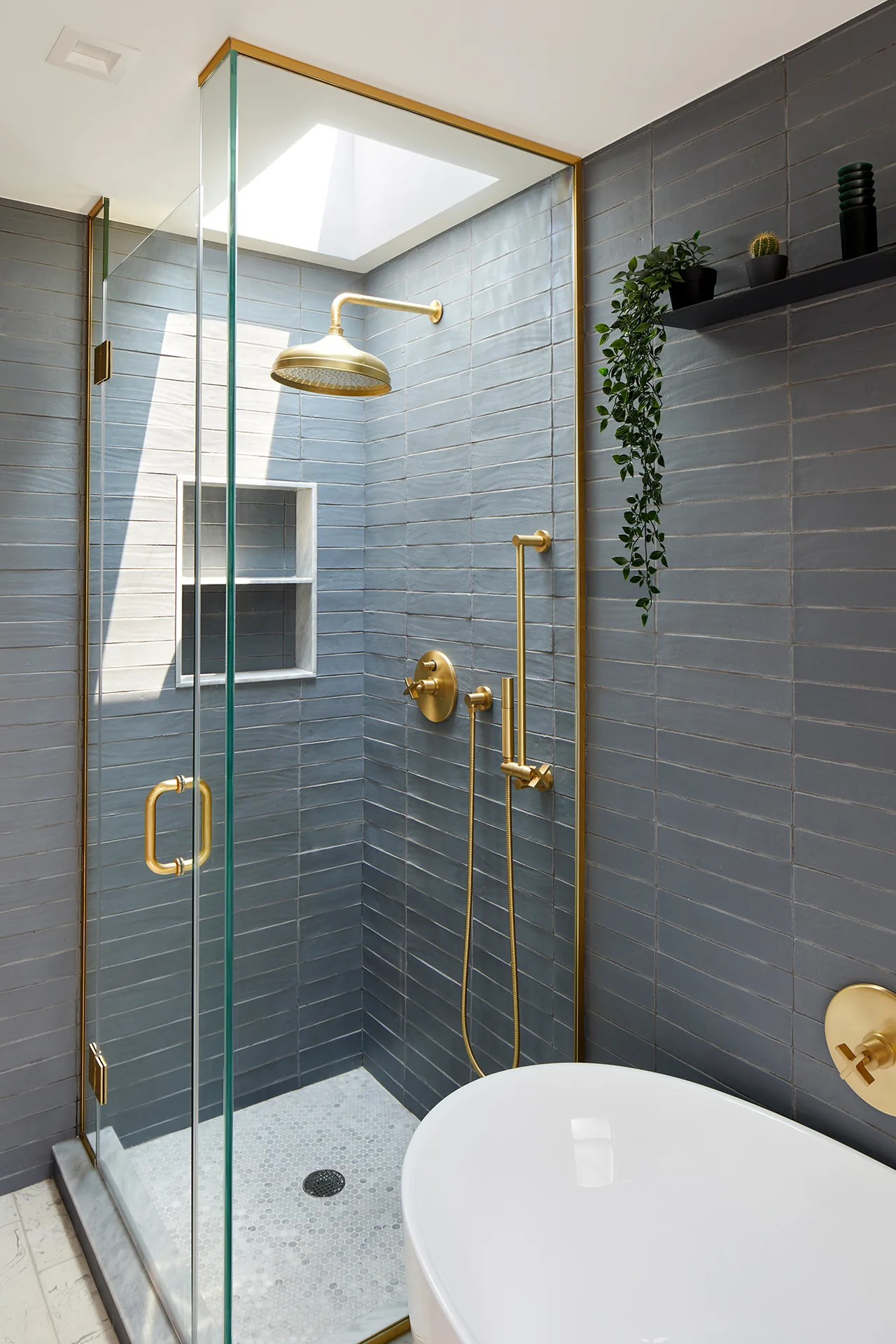 Modern bathroom shower with gold fixtures and gray tile walls, illuminated by a skylight, part of Greenpoint Residence by Krajewski Architect.