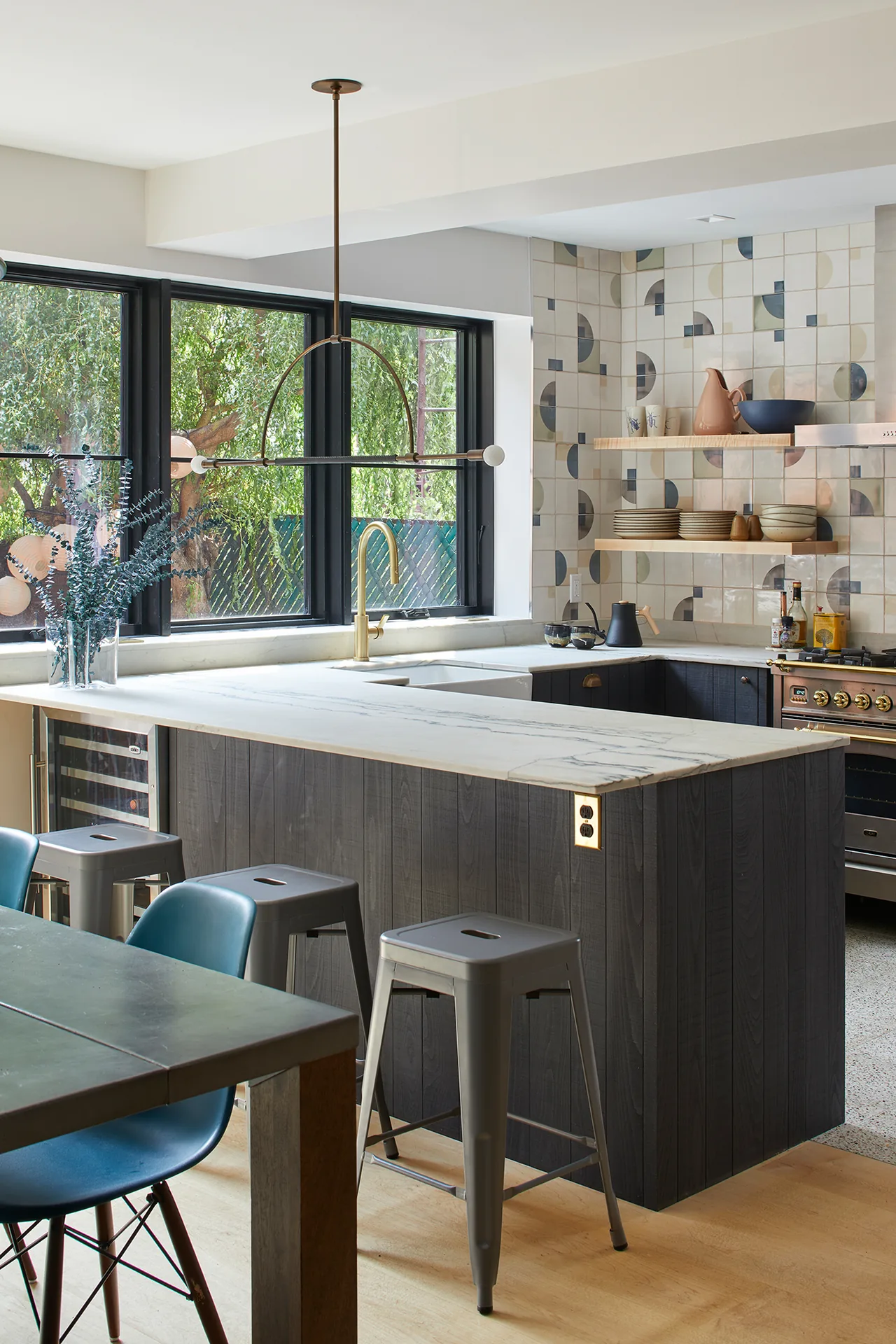 The Greenpoint Residence kitchen features a marble countertop, patterned tile backsplash, black cabinetry, and large black-framed windows.