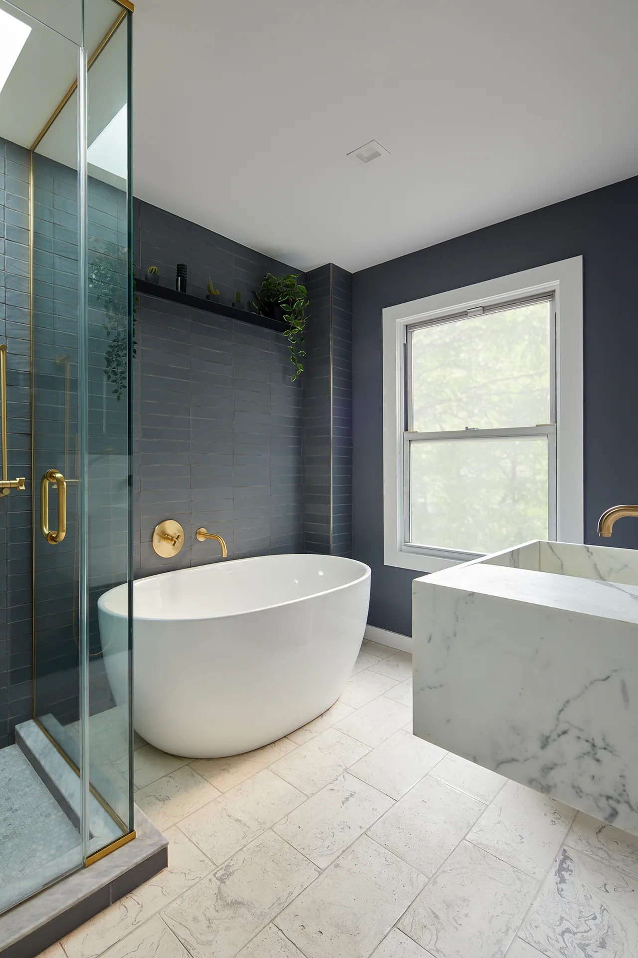 Bathroom featuring a freestanding tub, glass shower enclosure with brass hardware, marble sink, and dark tile walls.