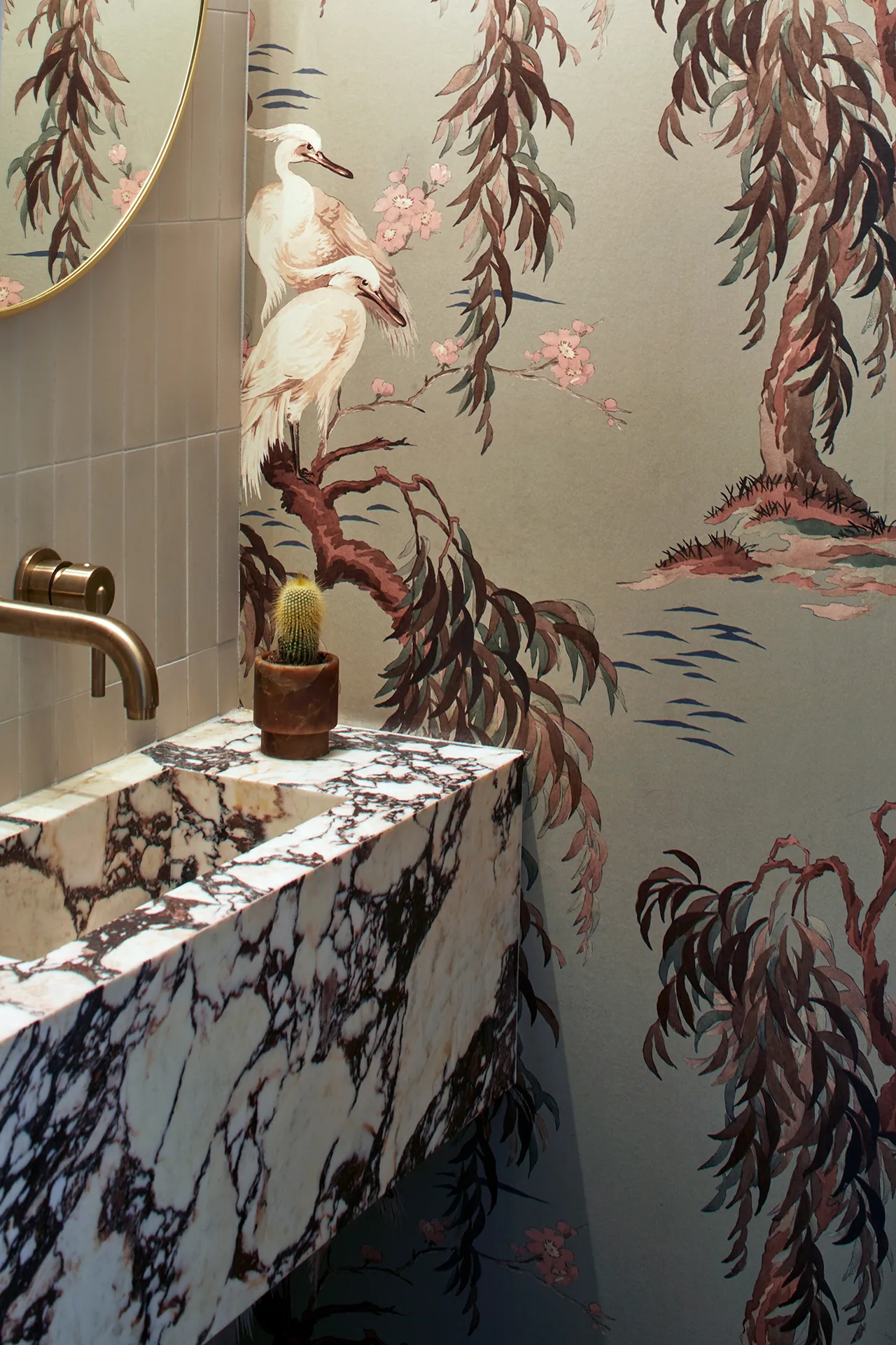 Marble vanity with integrated sink and brass faucet in a bathroom featuring nature-themed wallpaper.