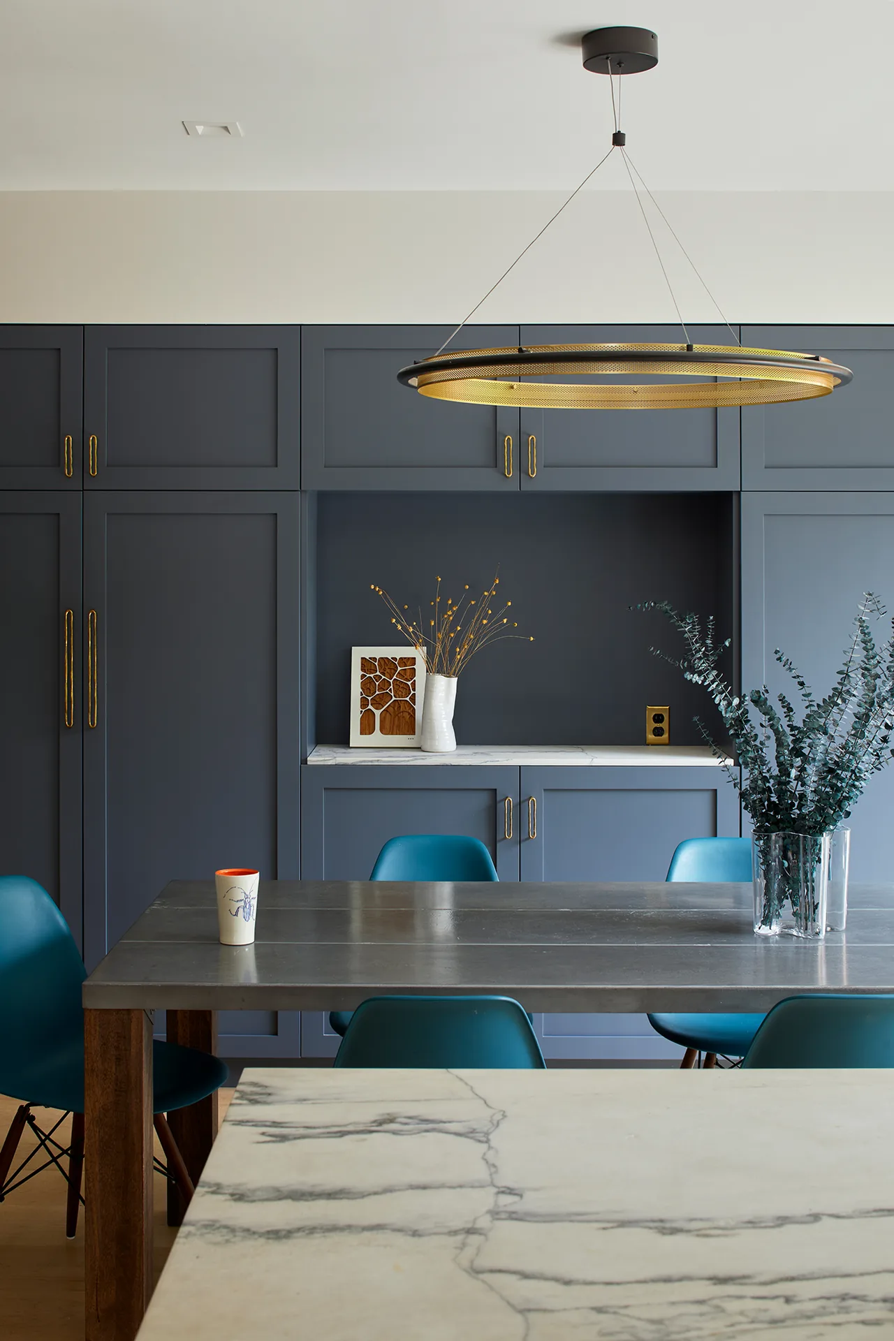 Dining area with blue chairs and built-in cabinetry featuring brass hardware and a large pendant light.