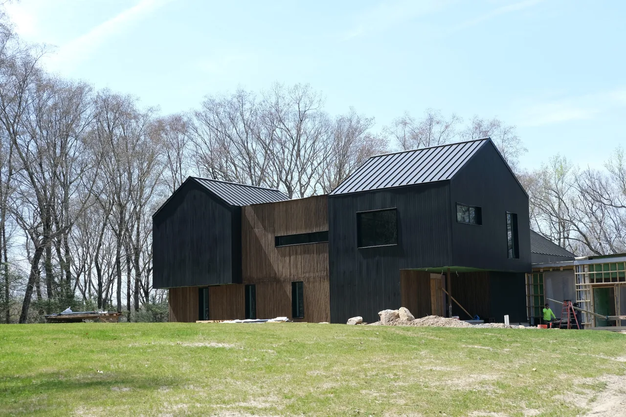 Side view of a modern two-story residence with dark vertical siding and metal gable roofs under construction.