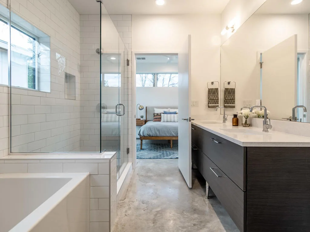 Bright bathroom features double sinks with dark wood cabinetry and a glass shower next to a tub.